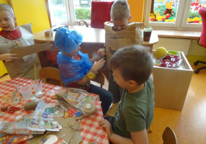 Czterech chłopców dekoruje stroje ekologiczne plastikowymi nakrętkami, kawałkami kartonów papierowych.
